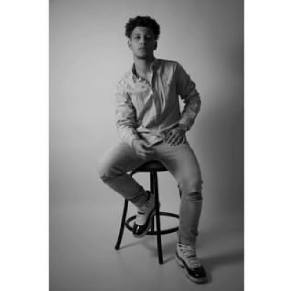 Black-and-white editorial portrait of Rome Rizzo seated on a studio stool